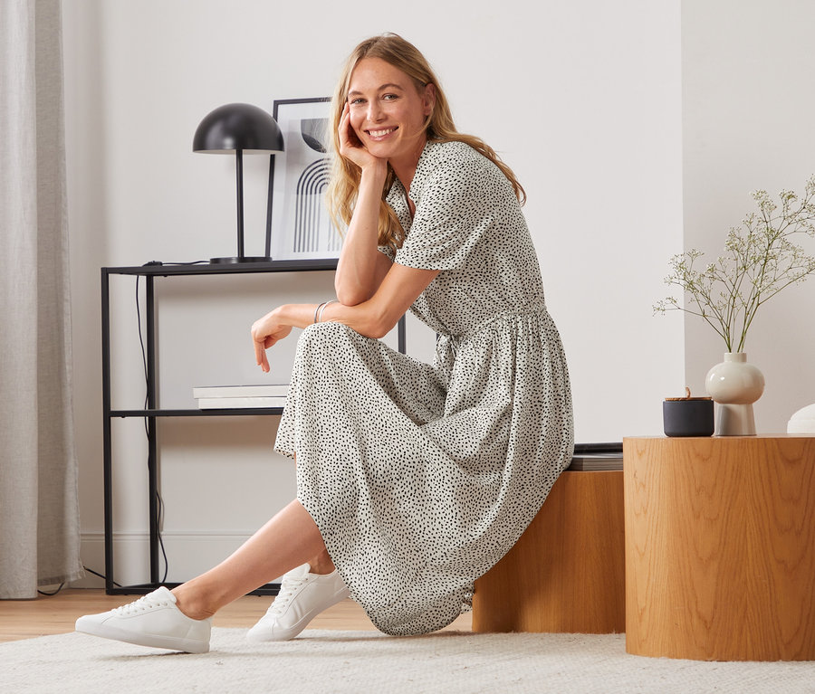 Frau sitzt auf einem Holzhocker und trägt ein Hemdblusenkleid.