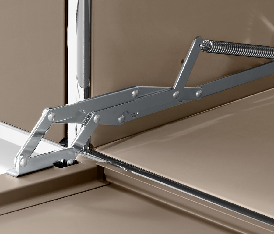 Detailaufnahme eines silbernen Klappmechanismus mit Feder auf einer braunen Oberfläche.