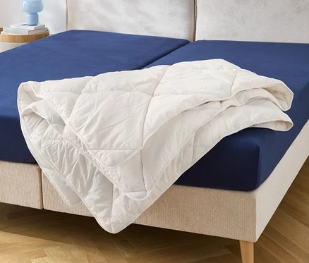 Auf einem Bett mit blauem Spannbettlaken liegt eine weiße Steppdecke.