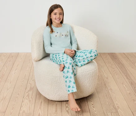 Mädchen sitzt in blauem Pyjama auf einem weißen, zotteligen Sessel.