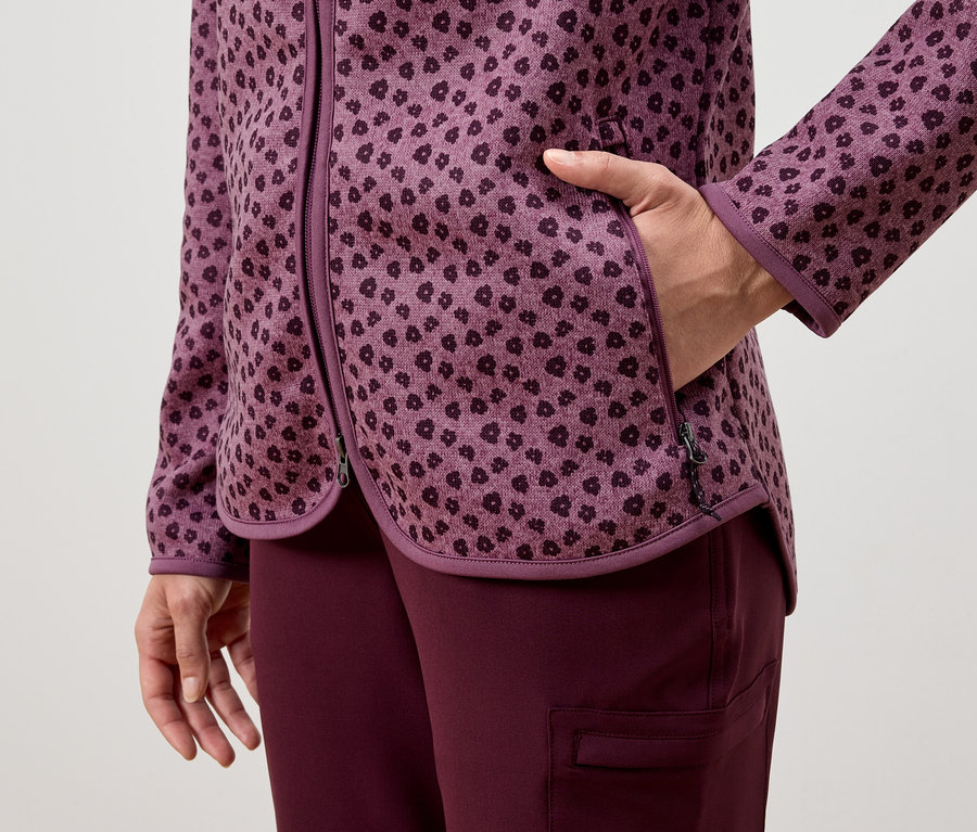 Frau hat ihre Hand in der Tasche einer lila gemusterten Jacke, getragen mit lila Hosen.