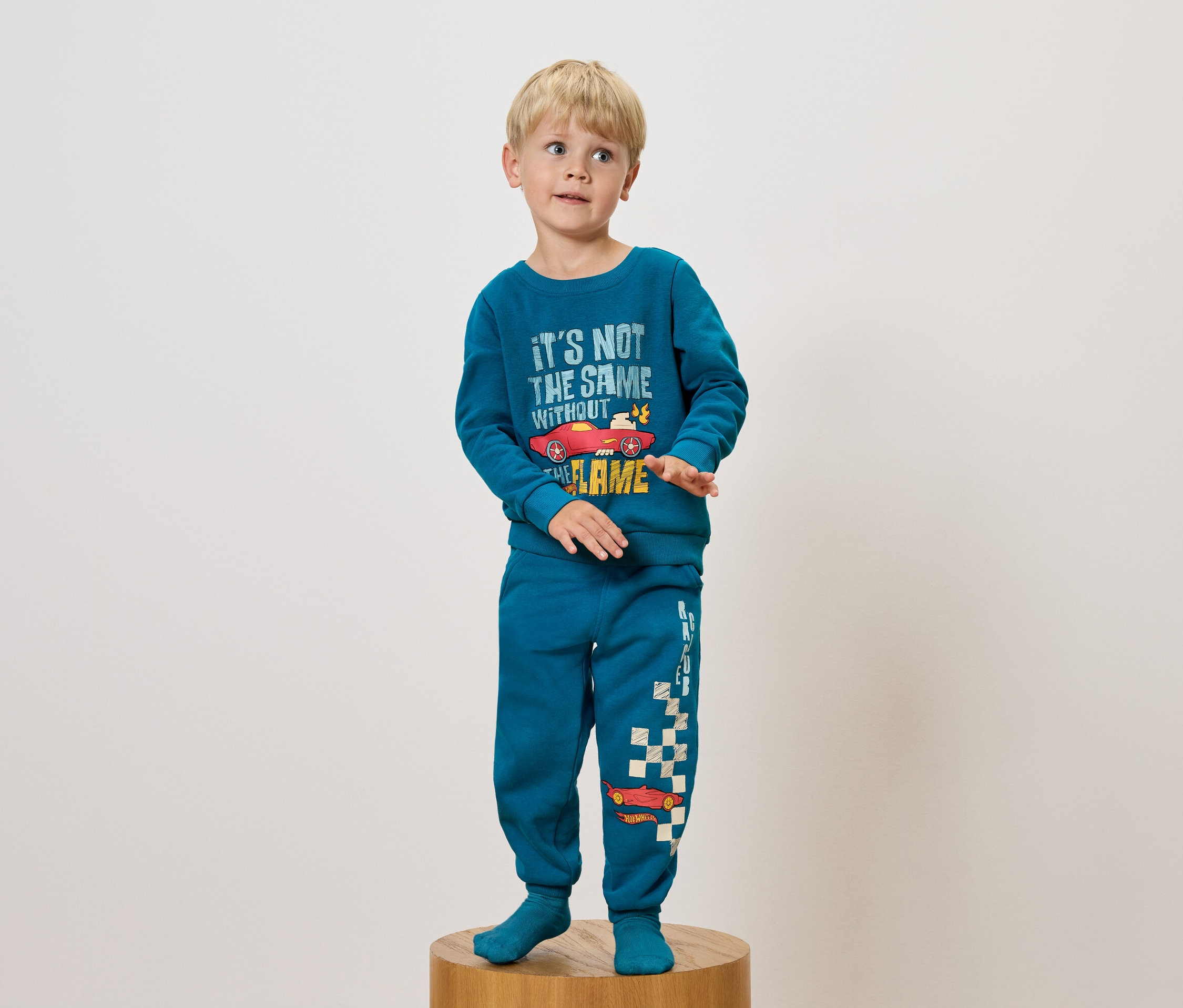 Junge im blauen Pyjama mit Autoaufdruck steht auf einem Holzsockel.