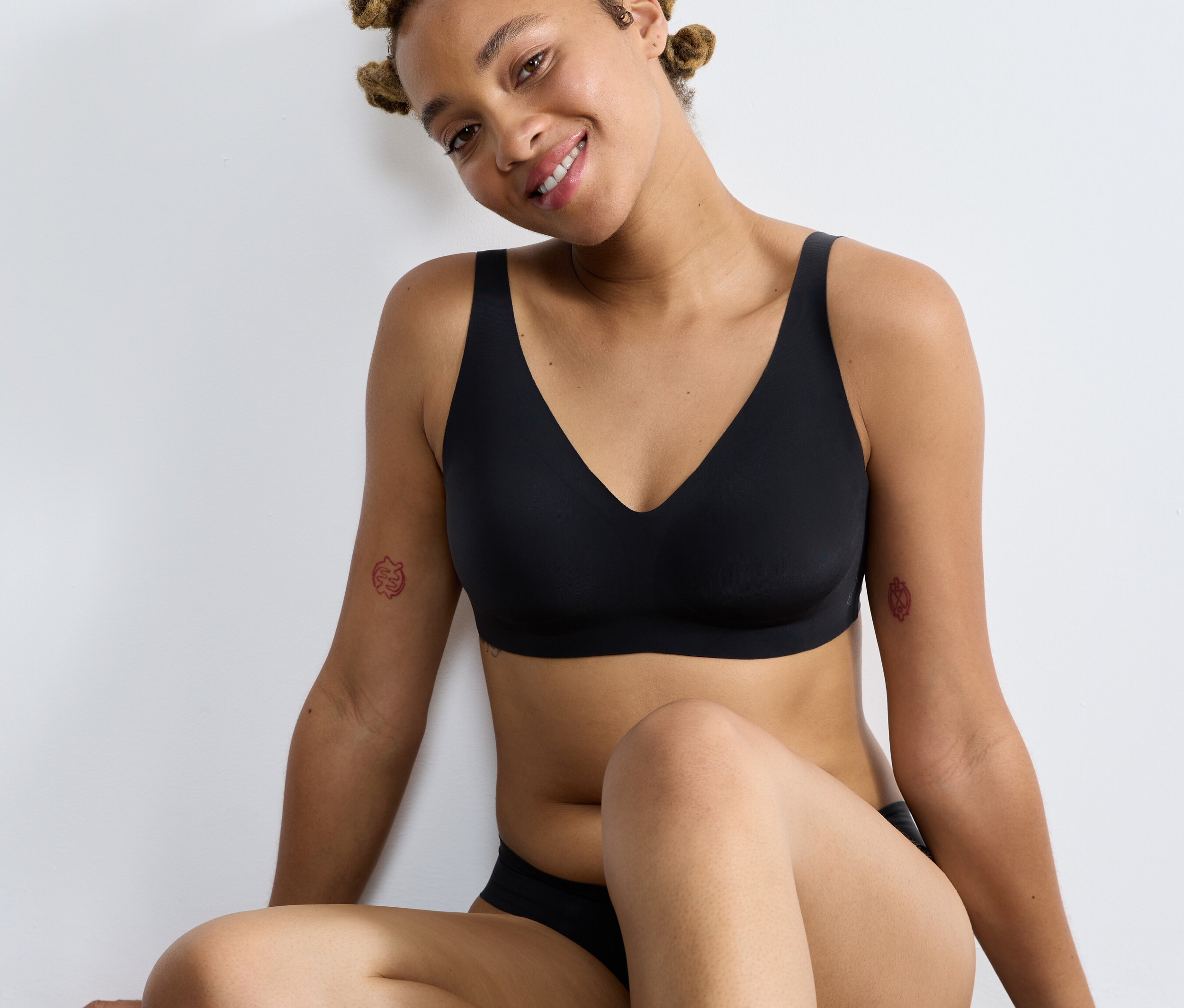 Frau sitzt und trägt einen schwarzen sloggi ZERO Feel 2.0 Soft Bra.