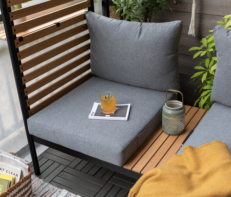 Graue Outdoor-Lounge mit Hocker, Glas mit Getränk und Laterne.