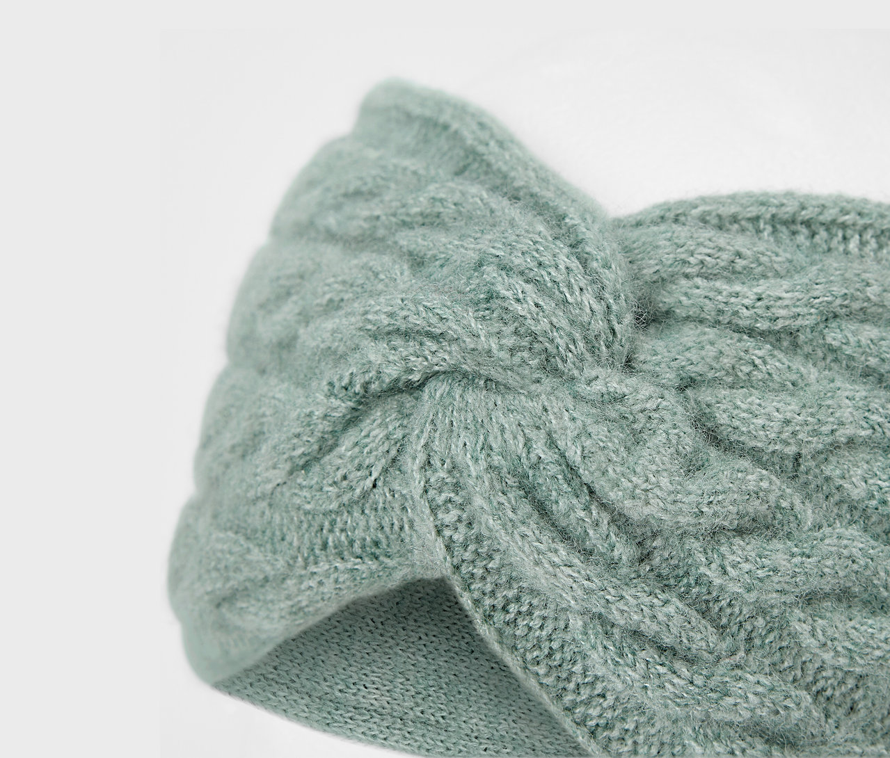 Nahaufnahme eines hellblauen, gestrickten Stirnbands mit Zopfmuster.