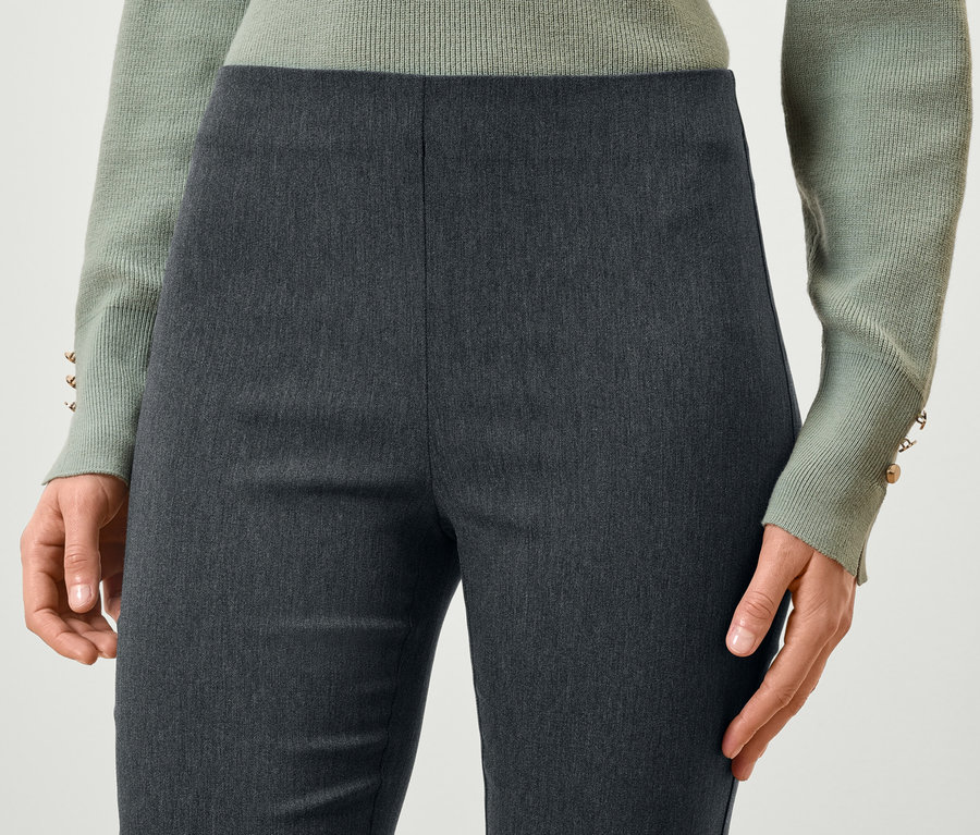 Detailaufnahme einer Frau, die graue Hosen und einen hellgrünen Pullover trägt.