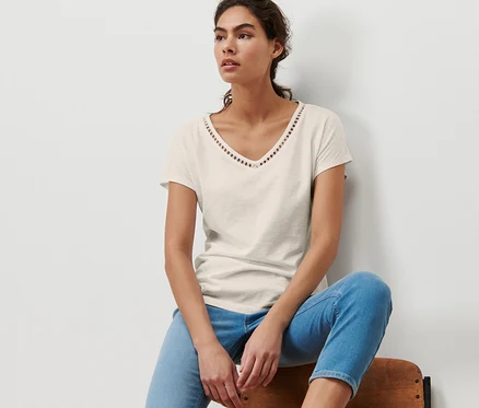 Frau sitzt auf einem Stuhl und trägt ein cremeweißes Shirt aus Modalmix.