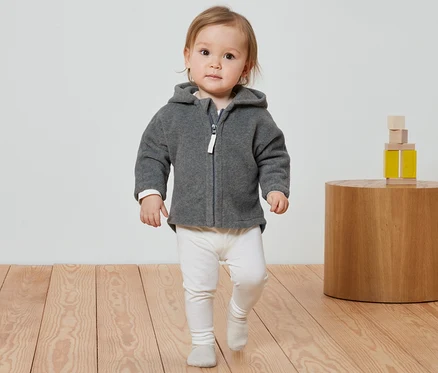 Kleinkind geht in grauer Baby-Fleecejacke und weißen Leggings.