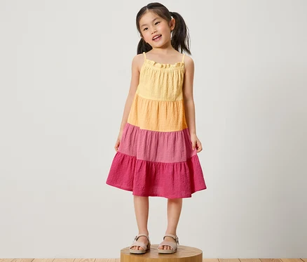 Mädchen steht auf einem Holzsockel und trägt ein Kinder-Webkleid.