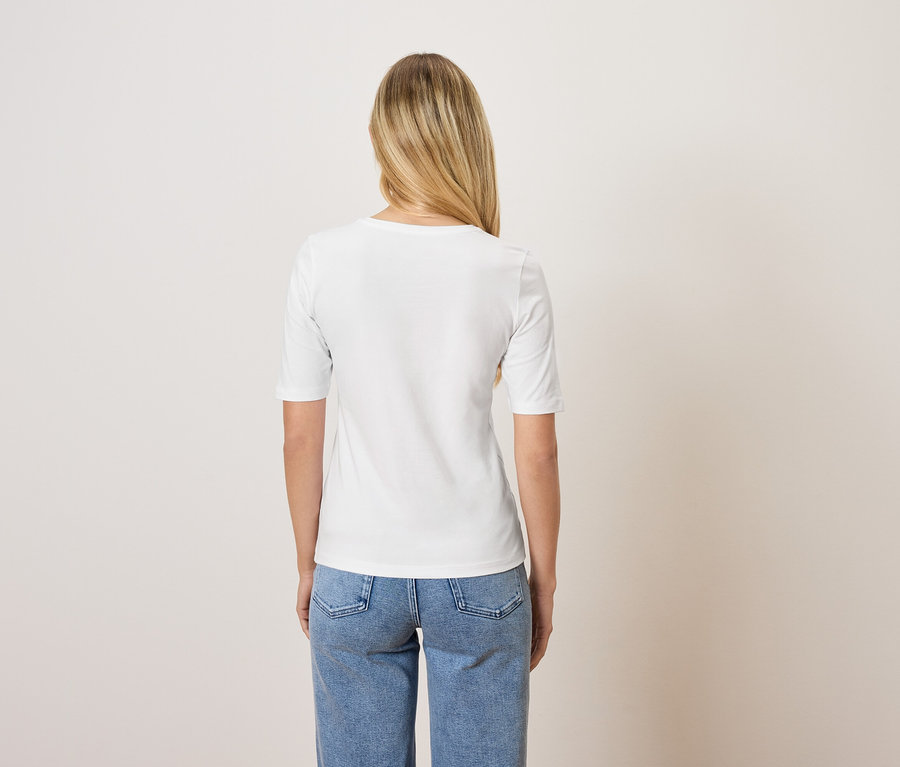 Rückansicht einer Frau mit blonden Haaren in einem weißen T-Shirt und blauen Jeans.
