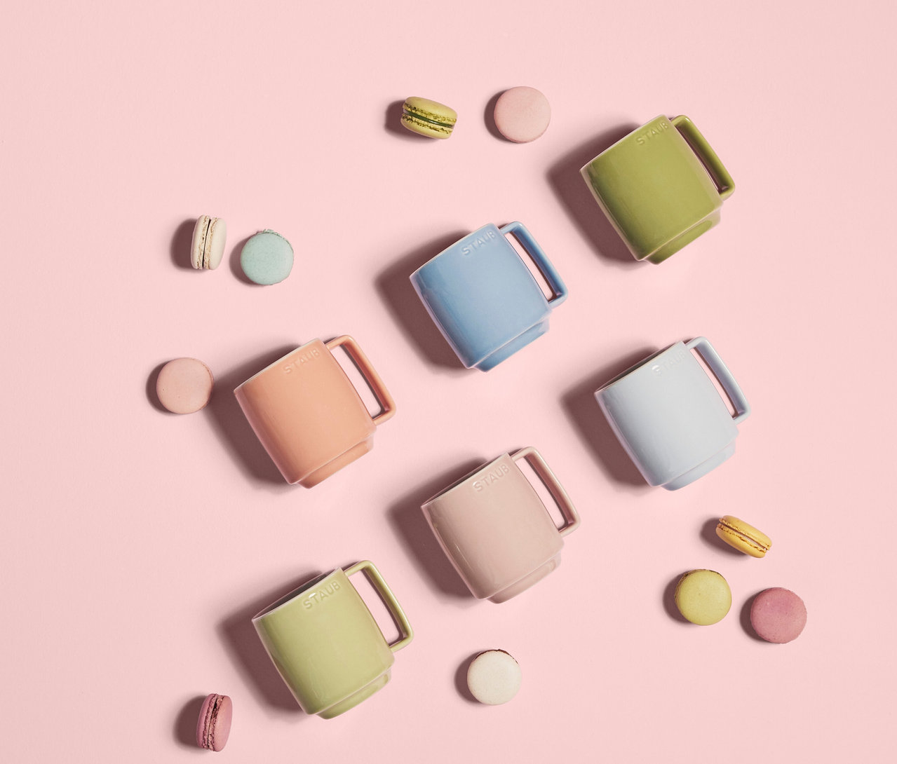 Draufsicht von sechs bunten STAUB Espressotassen »Macaron« und einigen Macarons auf rosafarbenem Hintergrund.