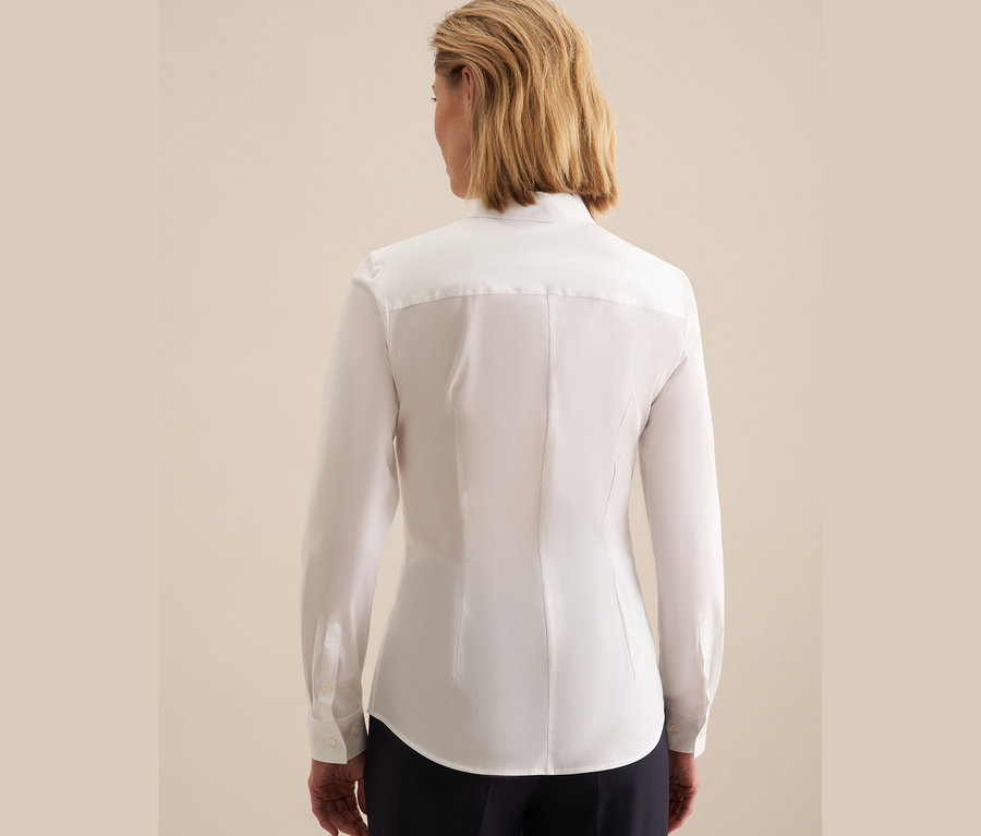 Rückansicht einer Frau mit kurzen blonden Haaren in einer weißen Seidensticker Slimfit Bluse und dunkelblauer Hose.