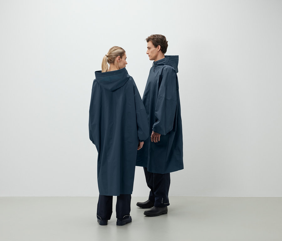 Ein Mann und eine Frau stehen einander gegenüber und tragen dunkelblaue Regenponchos mit Kapuze.