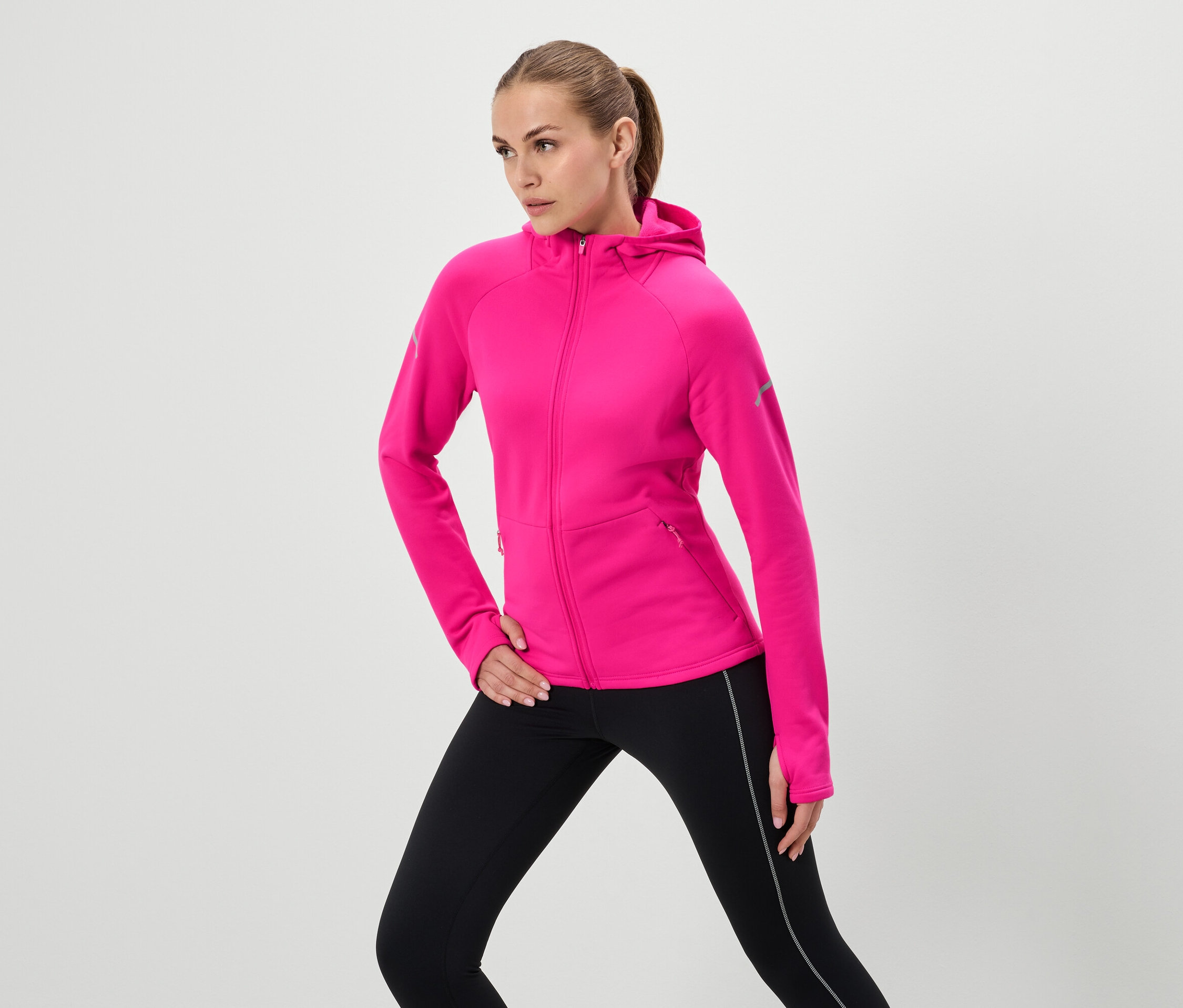 Frau posiert in pinkem Kapuzenpullover und schwarzen Leggings.