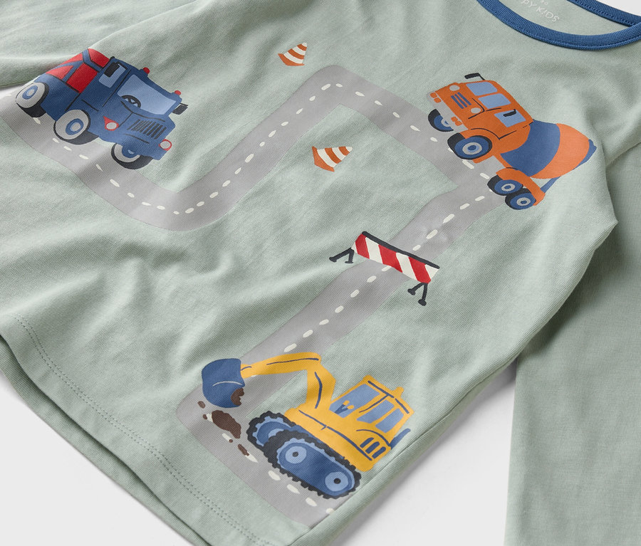 Auf einem hellgrünen Hemd sind Illustrationen von Baufahrzeugen auf einer grauen Straße abgebildet.
