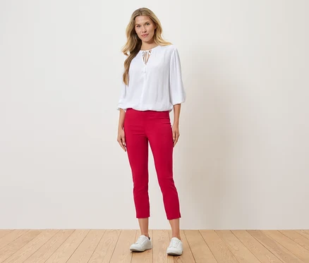 Frau steht und trägt eine weiße Bluse, rote Hose und weiße Turnschuhe.