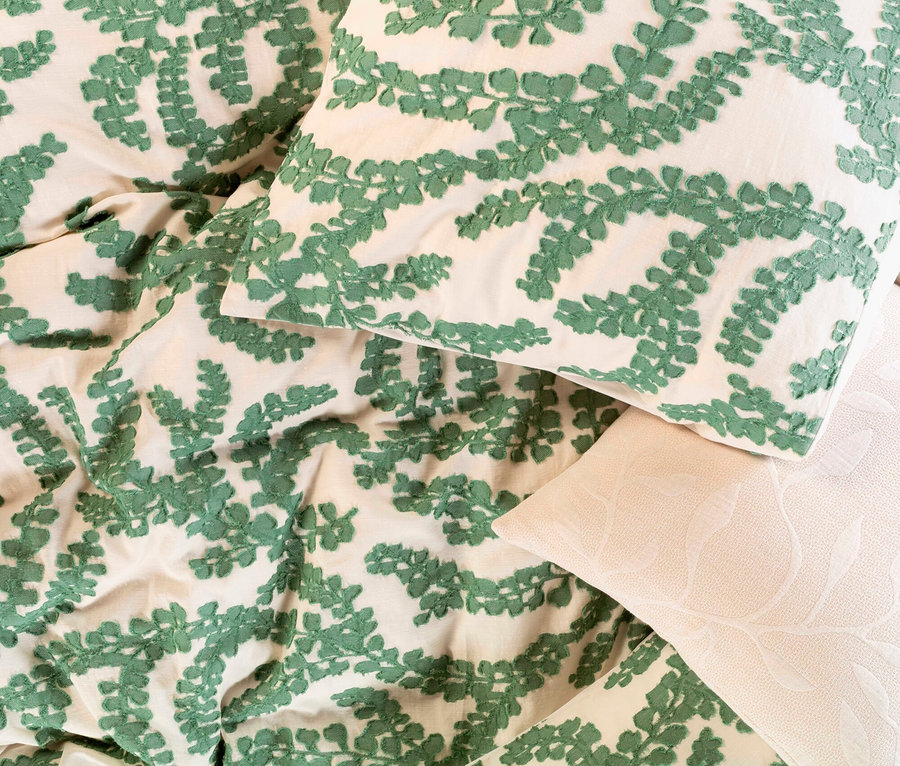 Nahaufnahme von Bettwäsche mit grünem Farnmuster auf weißem Grund.
