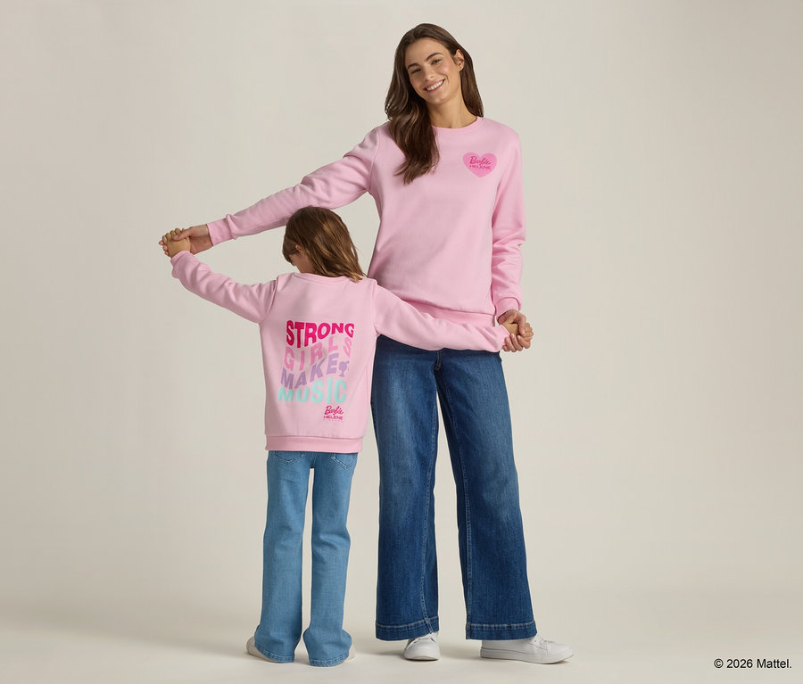 Eine Frau und ein Kind halten Händchen, beide tragen passende rosa Sweatshirts und Jeans.