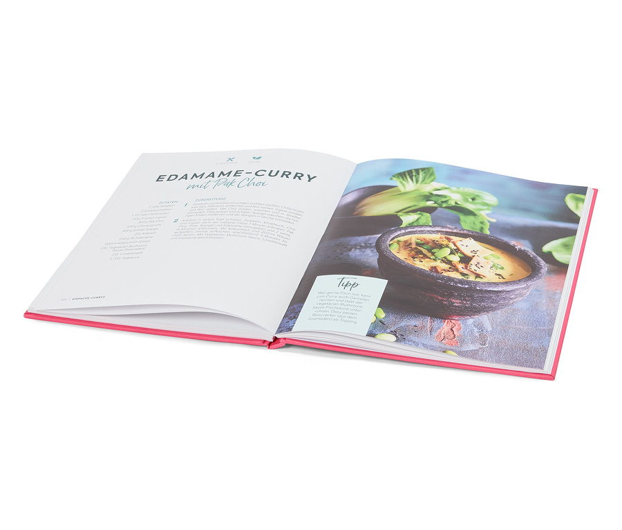 Aufgeschlagenes Kochbuch mit einem Rezept für Edamame-Curry mit Pak Choi, daneben ein Teller mit dem fertigen Gericht.