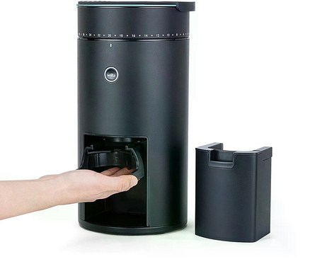 Eine Hand nimmt den Behälter aus einer schwarzen Wilfa-Kaffeemühle. Ein leerer Behälter steht daneben.