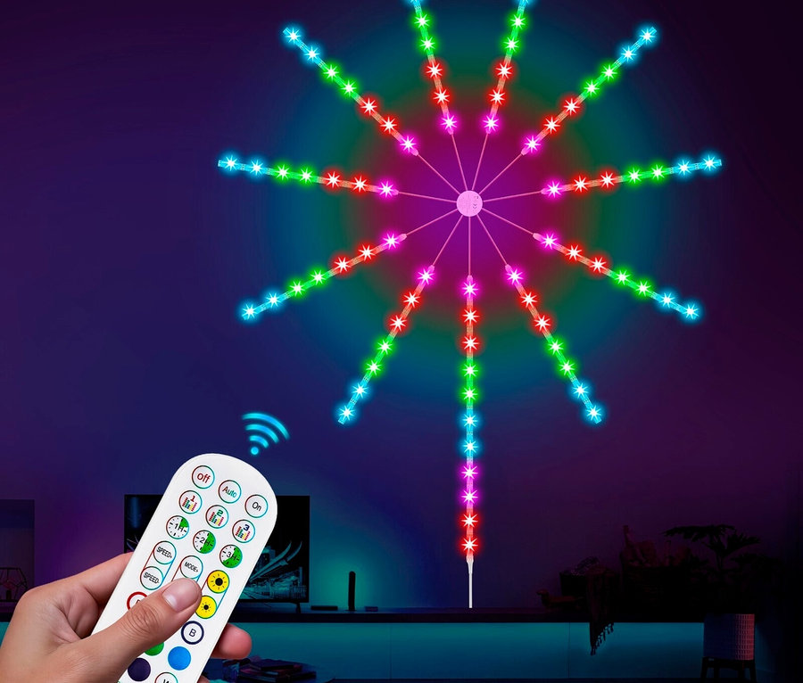 Eine Hand hält eine Fernbedienung vor einer bunten Feuerwerksleuchte an der Wand.