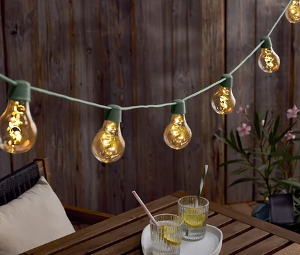 Lichterkette mit Glühbirnen hängt über einem Holztisch mit Getränken und einem Hut.