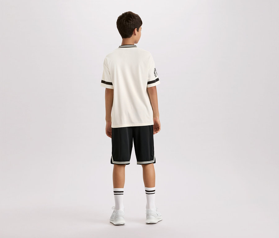 Rückansicht eines jungen Mannes in einem kurzärmeligen, cremefarbenen Hemd mit schwarzen Streifen am Kragen und an den Ärmeln, schwarzen Shorts mit weißen Streifen und weißen Socken und Schuhen.