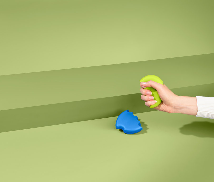 Hand drückt grünen Handtrainer, daneben liegt blauer 2 Handtrainer