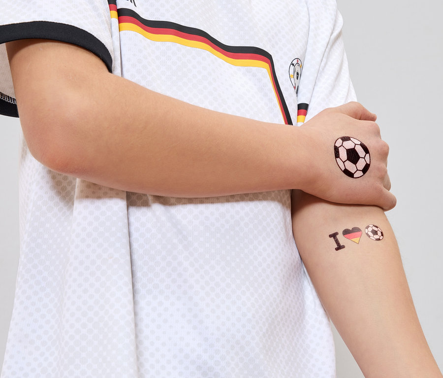 Person im Deutschlandtrikot mit Fußball-Tattoos auf Arm und Hand.