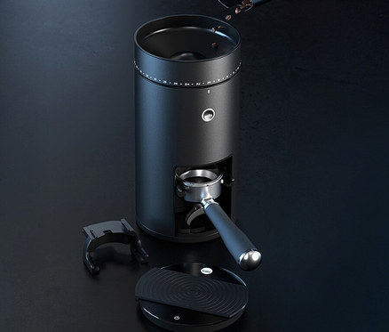 Eine schwarze Kaffeemühle mit Bohnen im Trichter, einem Siebträger und einer Waage auf einem dunklen Tisch.