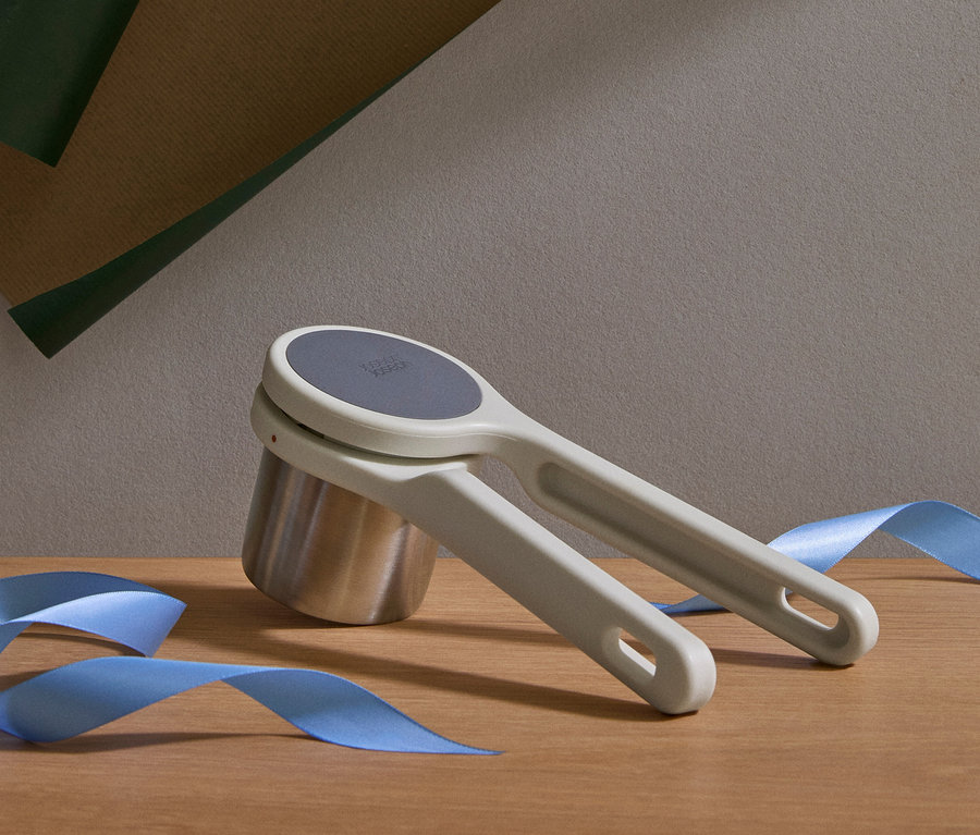 Ein grauer Küchenhelfer liegt auf einem silbernen Messbecher, daneben ein blaues Band.