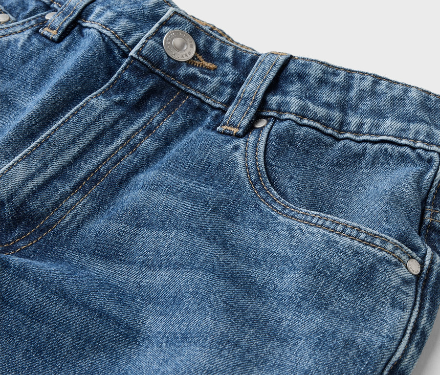 Detailaufnahme einer blauen Jeans mit Knopf, Gürtelschlaufe und Tasche vor einem weißen Hintergrund.