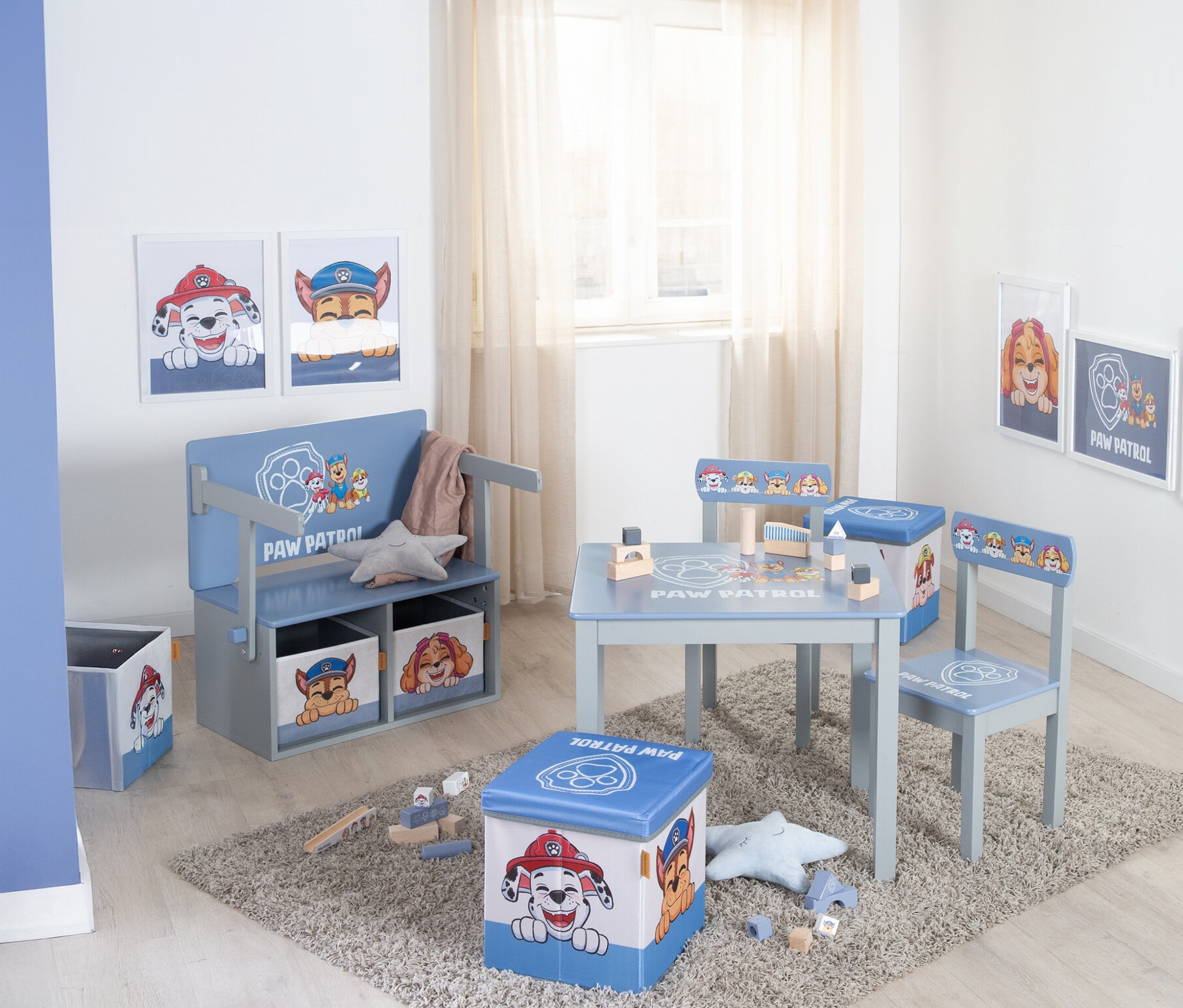 Ein Kinderzimmer mit hellblauen Paw Patrol-Möbeln, darunter ein Tisch mit Stühlen, eine Bank mit Aufbewahrungsboxen und eine Spielzeugkiste, auf einem grauen Teppich.