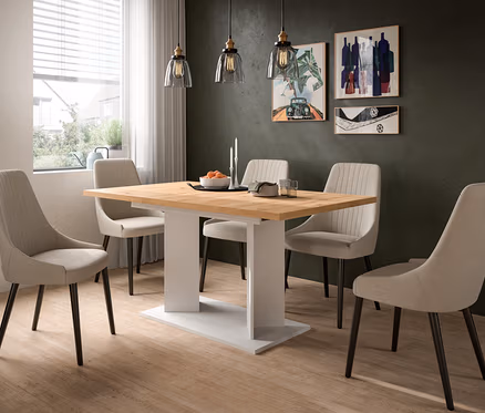 Ein modernes Esszimmer mit einem Holztisch und sechs beigen Stühlen. Auf dem Tisch stehen eine Obstschale, Kerzen, Teller und Gläser. Eine dunkelgrüne Wand mit drei Bildern und drei Pendelleuchten ist im Hintergrund zu sehen.
