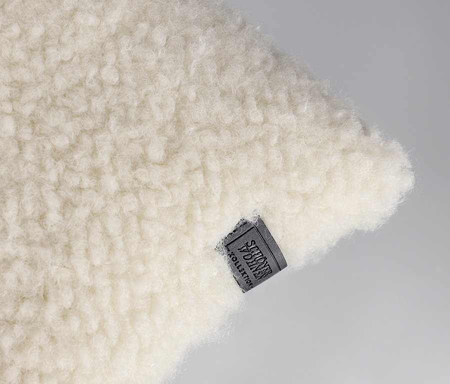 Nahaufnahme eines offwhite, flauschigen SCHÖNER WOHNEN-Kollektion Dekokissenbezugs »TEDDY« mit einem dunkelgrauen Etikett.