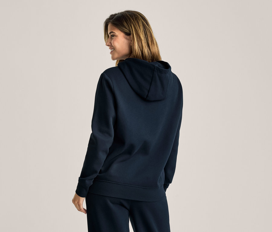 Frau von hinten, leicht zur Seite gedreht, lächelt und trägt einen dunkelblauen Kapuzenpullover und eine passende Jogginghose.