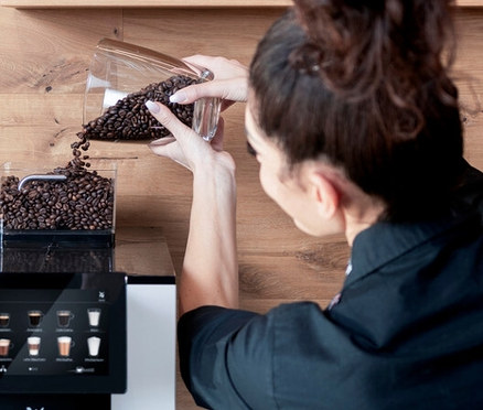 Frau füllt Kaffeebohnen in einen Profi-Kaffeevollautomat »WMF 950 S«.