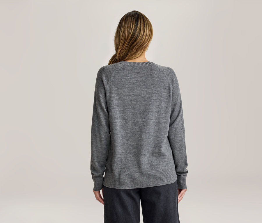 Frau von hinten, trägt ein graues Langarmshirt und dunkle Hosen. Ihr langes, hellbraunes Haar fällt über ihre Schultern.