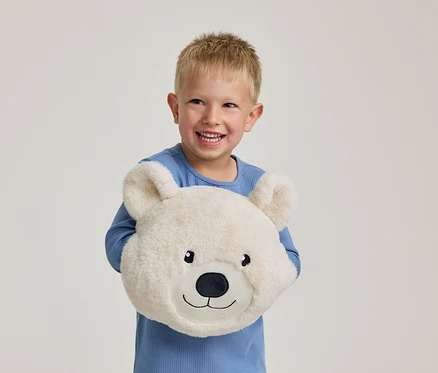 Ein lächelnder kleiner Junge in einem blauen Oberteil hält ein flauschiges, weißes Bärenkissen.