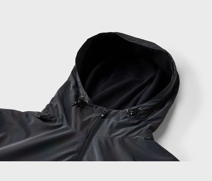 Nahaufnahme einer dunklen, möglicherweise irisierenden Jacke mit Kapuze. Die Kapuze ist mit schwarzem Fleece gefüttert und hat verstellbare Kordelzüge. Ein schwarzer Reißverschluss ist vorne sichtbar.