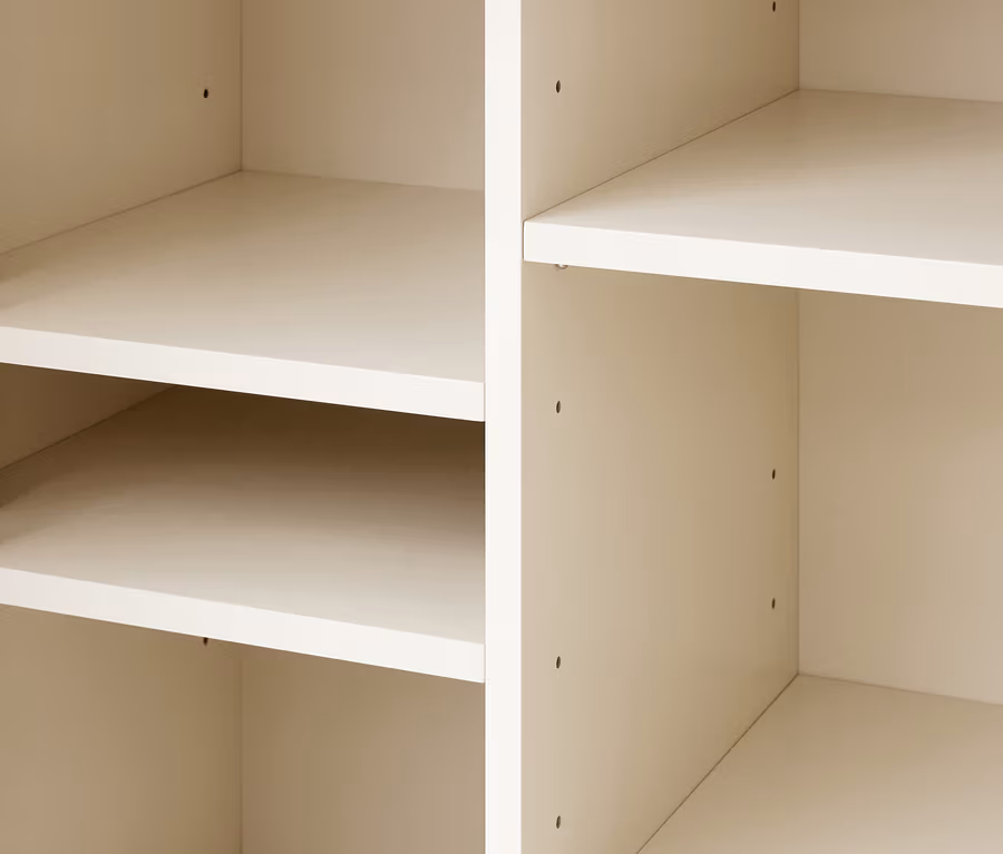 Nahaufnahme von leeren, hellbeigen Regalfächern mit sichtbaren Löchern zur Regalhöhenverstellung.