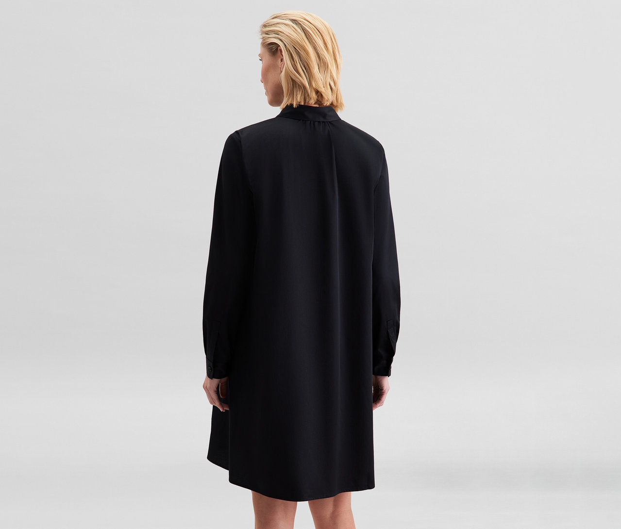 Frau mit kurzen blonden Haaren, von hinten gesehen, trägt ein schwarzes langärmeliges Kleid.