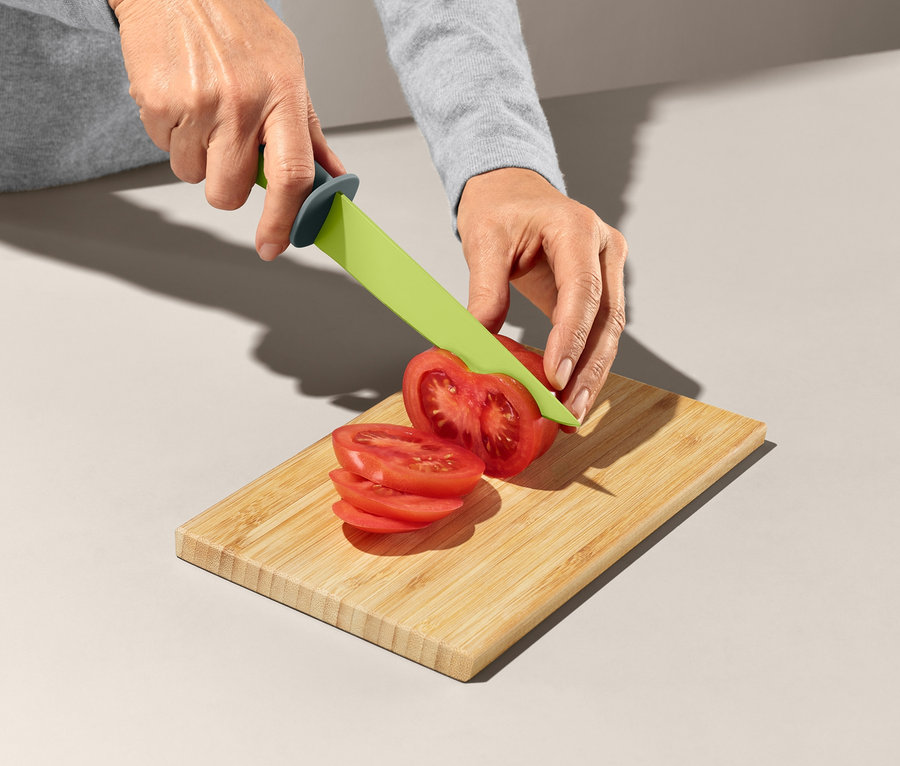 Frau schneidet Tomate mit grünem Messer aus Küchenhelfer-Set auf Holzbrettchen.