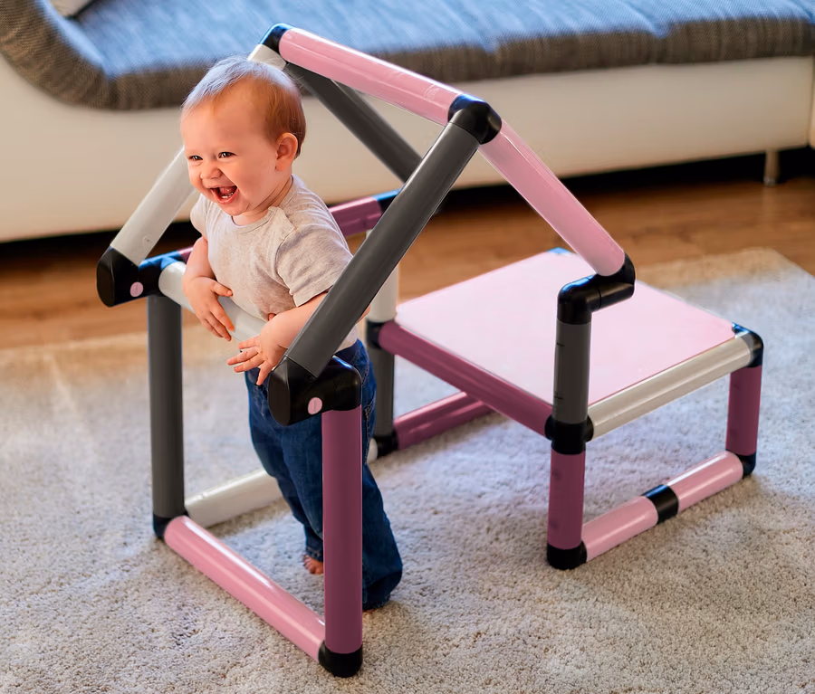 Ein lachendes Baby steht im Quadro-Home-BEGINNER-Set mit rosa, grauen und weißen Rohren.