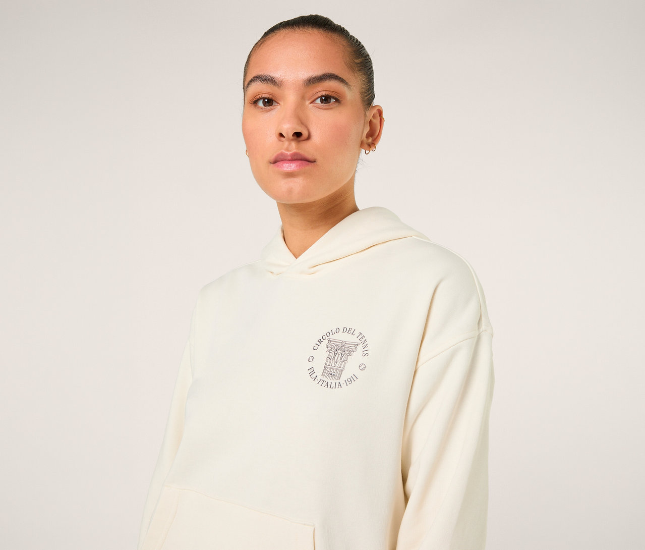Frau trägt einen offwhite FILA Damen-Hoodie »MARLIA« mit einem runden Logo auf der Brust.