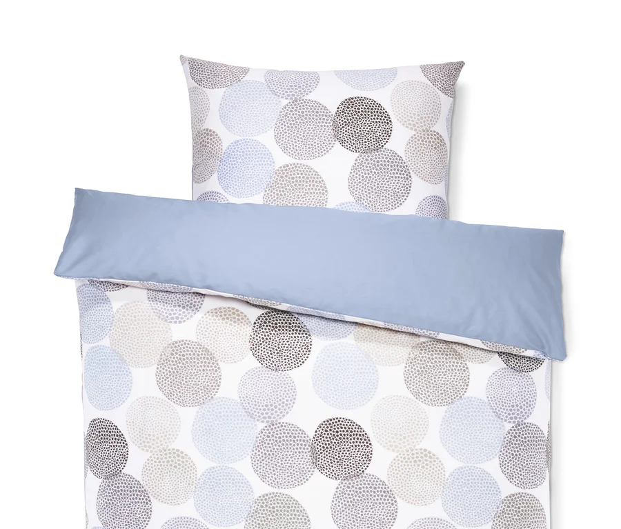 Auf einem weißen Hintergrund liegt eine Satin-Wendebettwäsche in Normalgröße mit blauem Rand und einem Muster aus gepunkteten Kreisen.