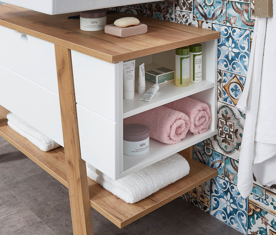 Weißer Waschbecken-Unterschrank »Novolino« mit Holzplatte und offenen Regalen mit Kosmetika und Handtüchern.
