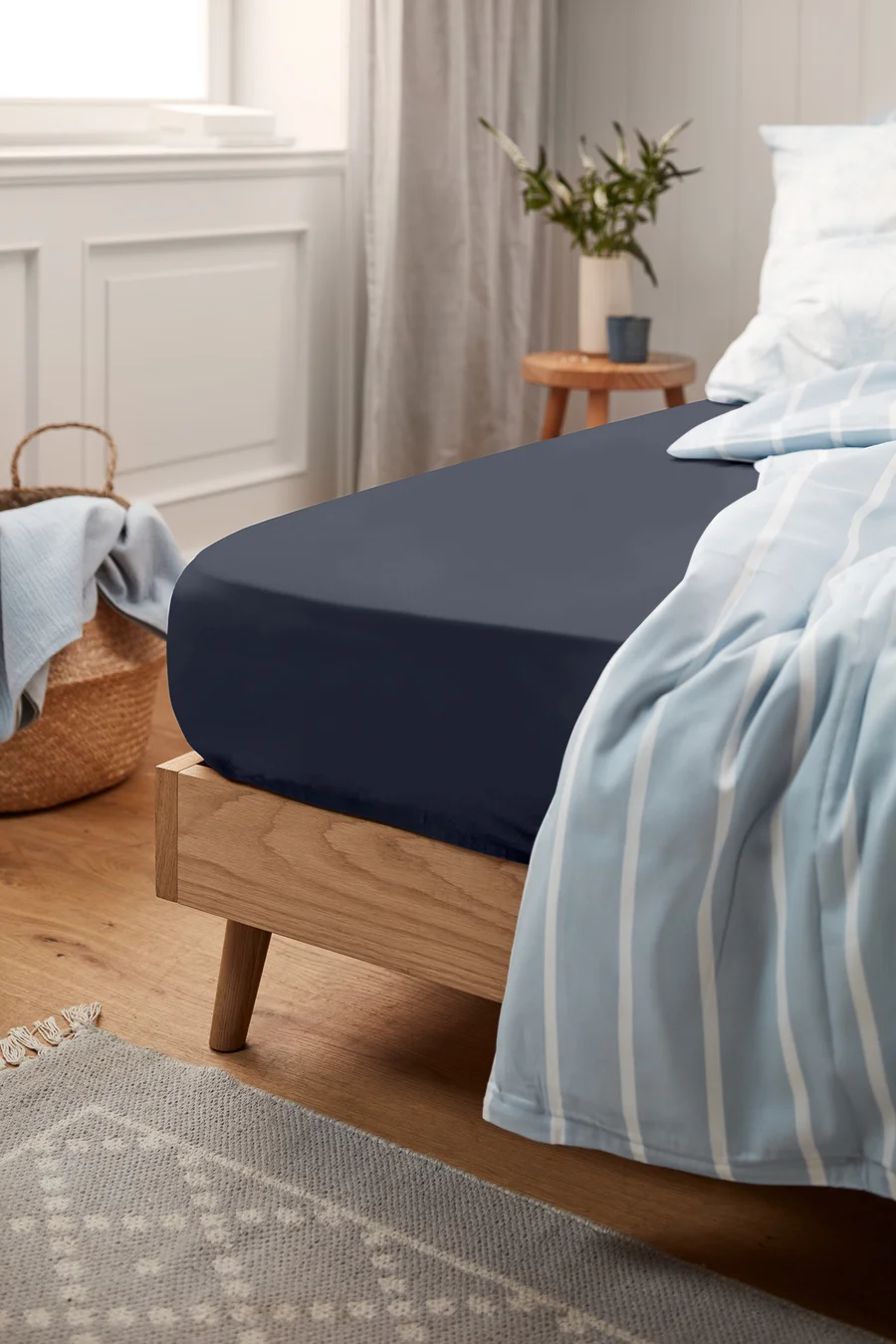 Ein marineblaues Jersey-Spannbettlaken auf einem Bett mit einer blau-weiß gestreiften Tagesdecke.