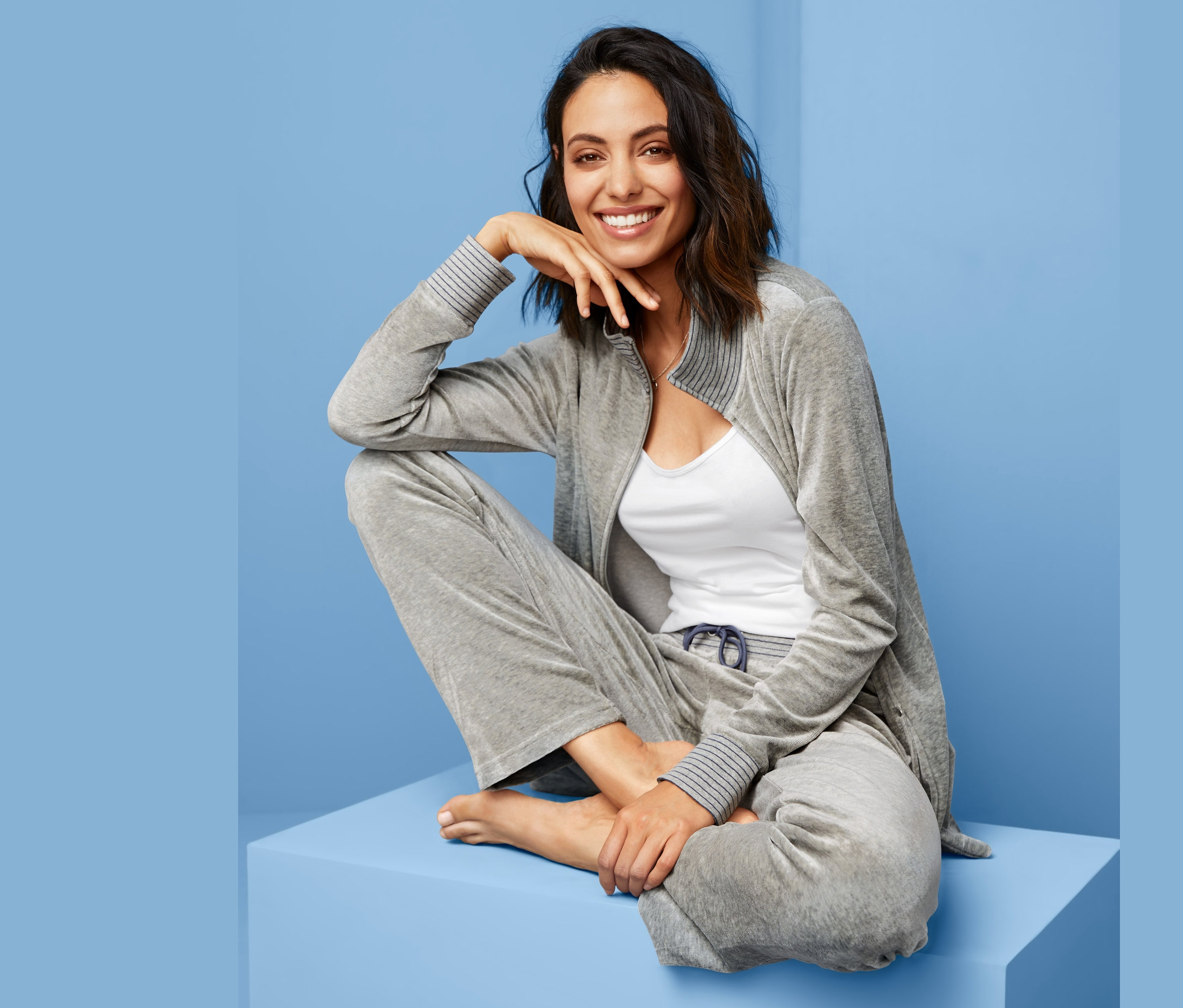 Frau sitzt auf einem blauen Block und trägt einen grauen Nicki-Hausanzug.