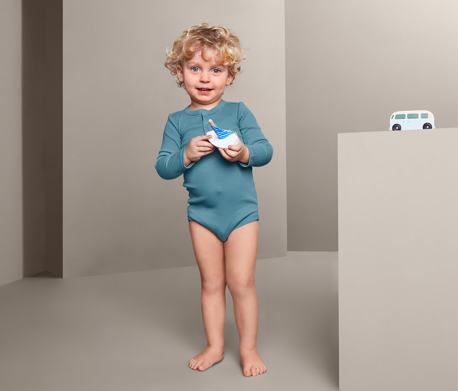 Kleiner Junge hält ein Spielzeug in den Händen und trägt einen 3er Langarmbody.